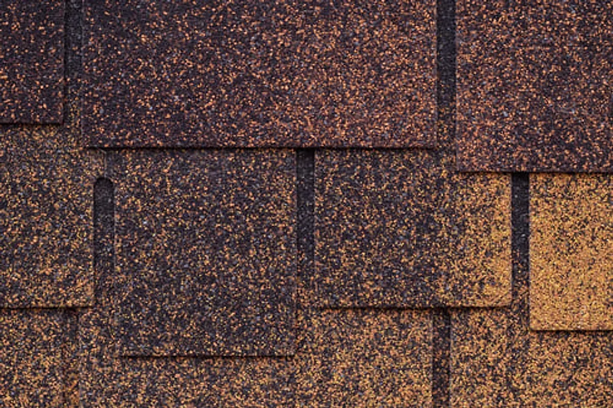 Close-up of storm-damaged asphalt shingles with bruising and granule loss